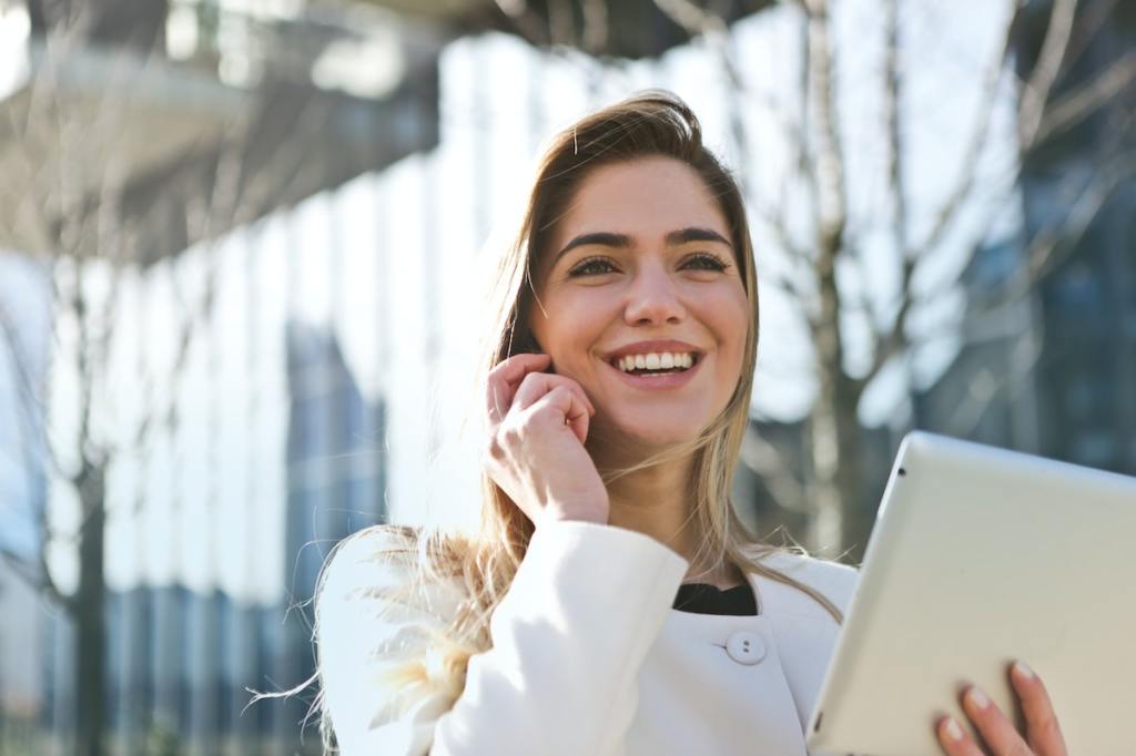 Eine blonde Frau mit einem zusammengefalteten Notebook in der Hand telefoniert draußen