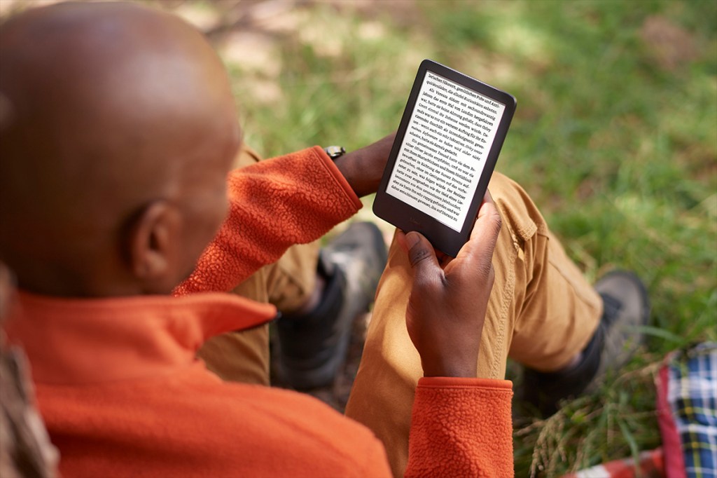 Ein Mann liest mit dem Amazon Kindle (2022) auf einer Wiese ein Buch.