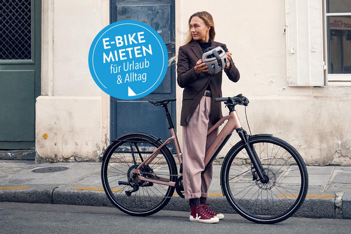 Frau steht an Straße mit einem E-Bike