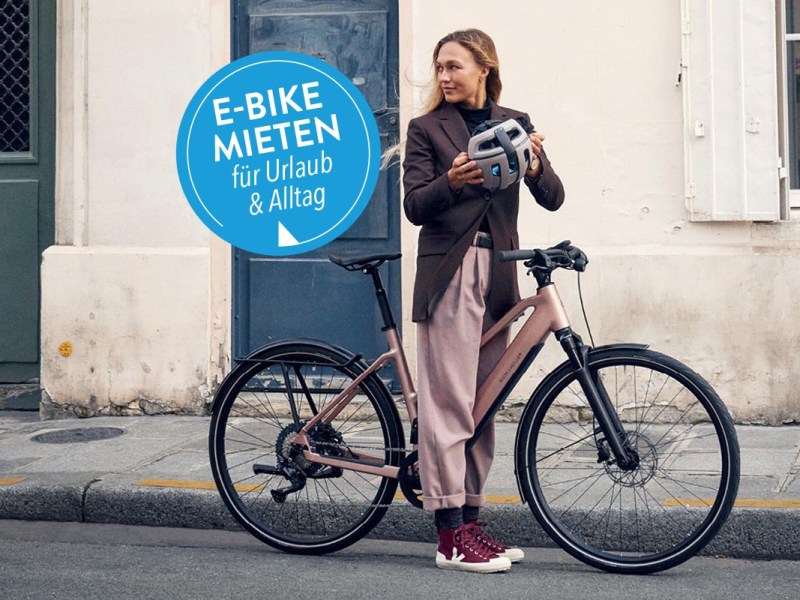 Frau steht an Straße mit einem E-Bike
