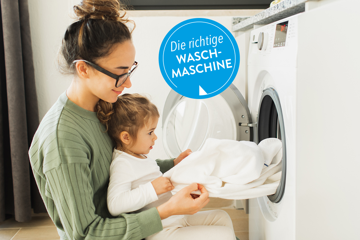 Frau mit Kind räumt Wäsche aus einer Waschmaschine.