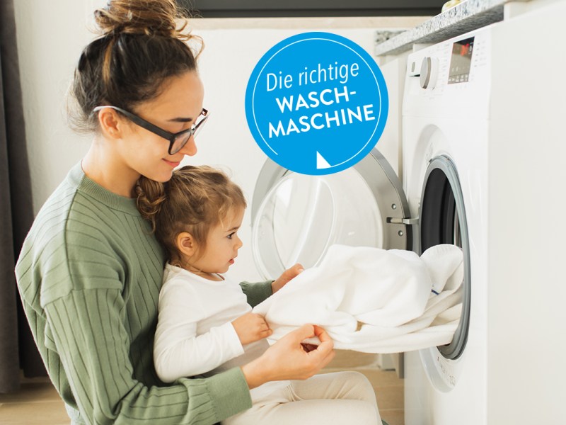 Frau mit Kind räumt Wäsche aus einer Waschmaschine.
