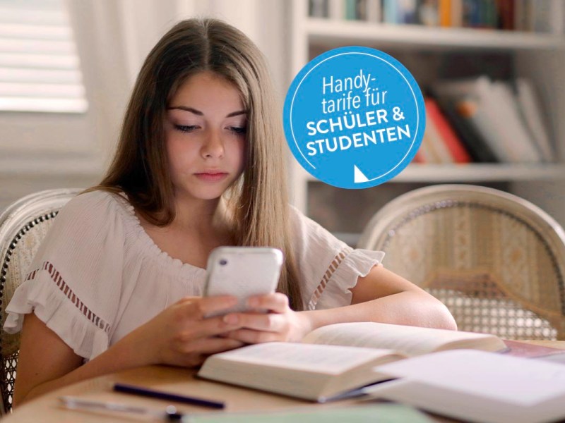 Mädchen sitzt am Tisch mit einem Handy in der Hand.