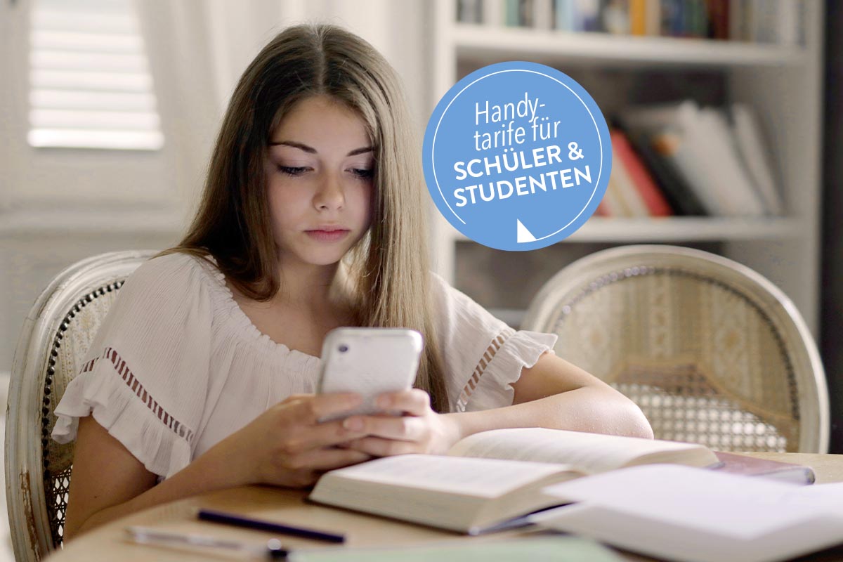 Mädchen sitzt am Tisch mit einem Handy in der Hand.