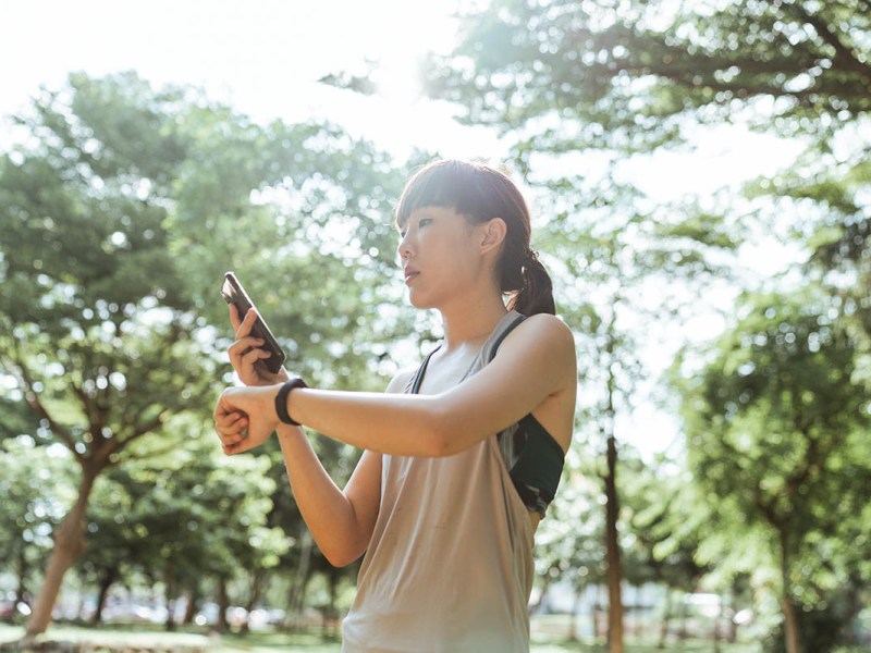 Eine Frau sieht auf ihr Handy sowie ihren Fitnesstracker.