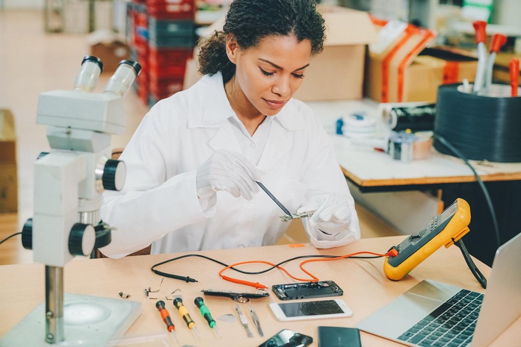 Eine Technikerin im weißen Kittel repariert ein Smartphone an einem Tisch