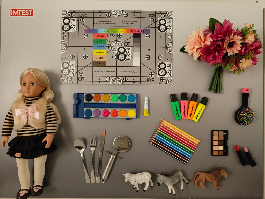 Aufnahme vom Testchart mit Messfeldern und plastischen Objekten, wie einer Puppe, Blumenstrauß und Buntstiften