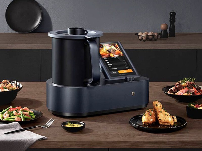 Der neue Mijia Cooking Robot steht in einer Küche. Um ihn herum stehen verschiedene Speisen.