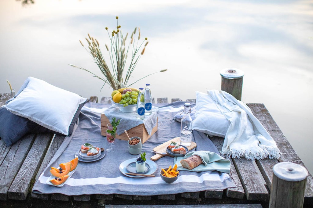 Auf einem Steg an einem See ist ein Picknick aufgedeckt.