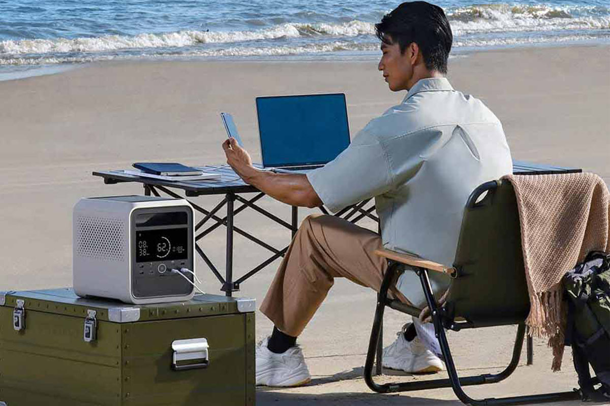 Eine Person arbeitet an einem Schreibtisch am Strand. Daneben steht die neue Xiaomi Mijia 1000 Pro Power Station.