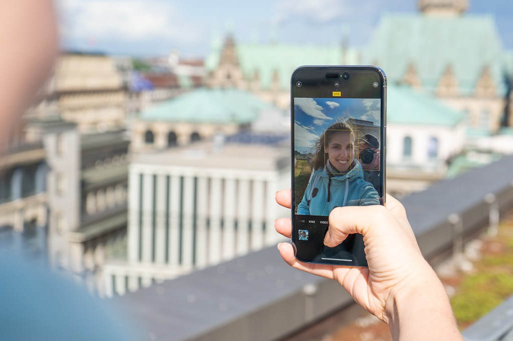 Selfie der Redakteurin mit iPhone vor städtischem Hintergrund