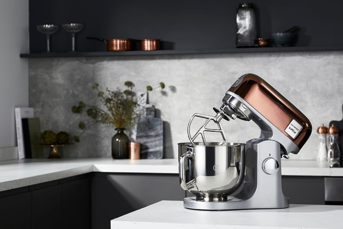 Silbern Bronzene Kenwood K-Mix Küchenmaschine auf weißer Kücheninsel vor weiß schwarzer Küche