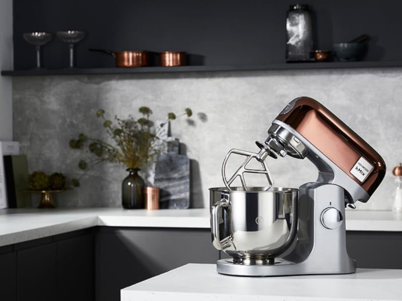 Silbern Bronzene Kenwood K-Mix Küchenmaschine auf weißer Kücheninsel vor weiß schwarzer Küche
