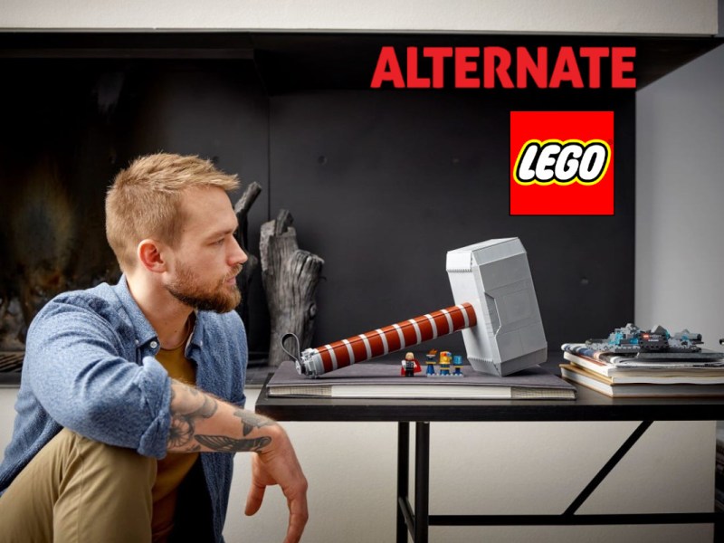 mann sitzt vor Tisch auf dem LEGO Nachbildung von Thors Hammer steht mit Lego Logo und Alternate Logo rechts
