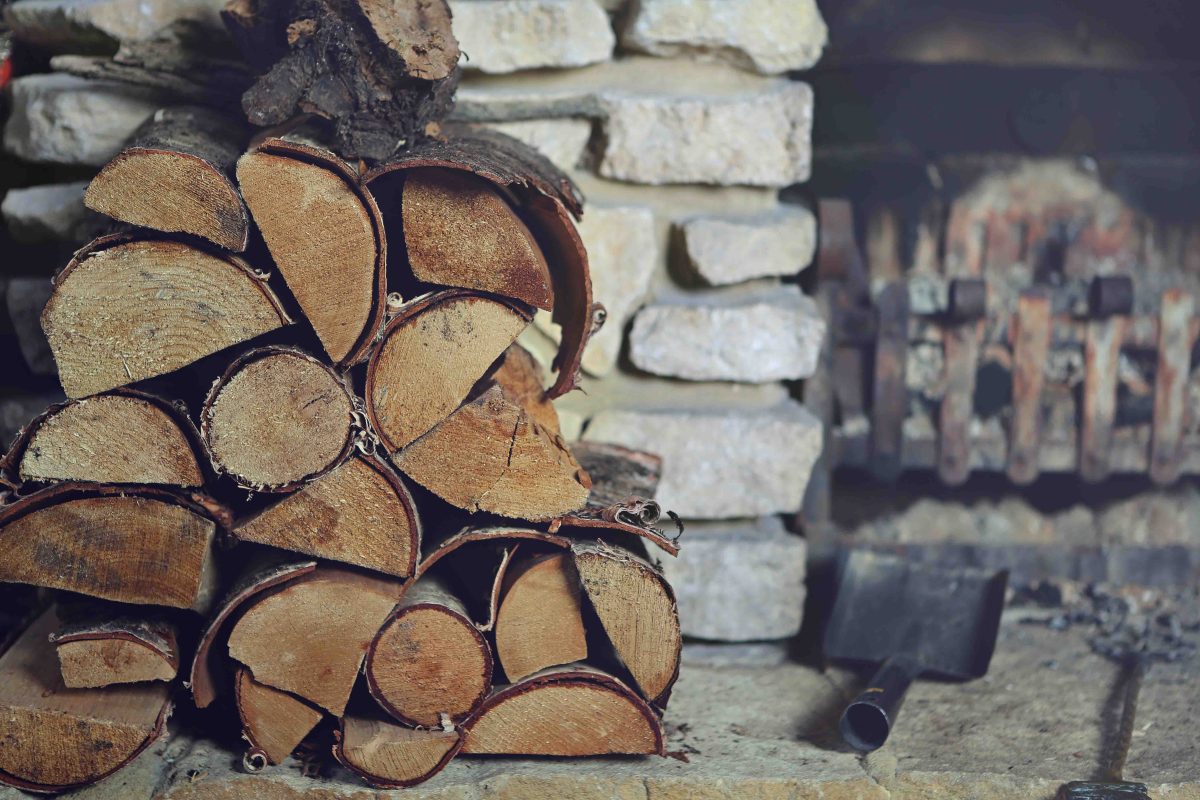 Ein Stapel mit Holzscheiten neben einem offenen Kamin.