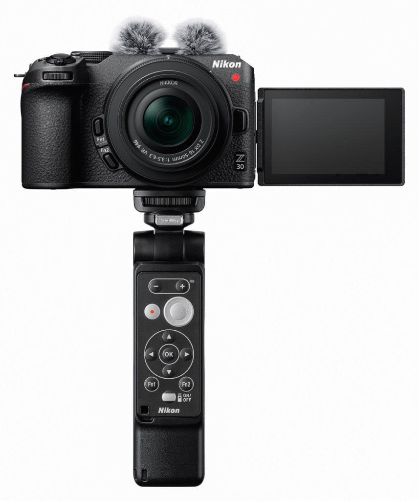 Schwarze Kamera auf Stativ mit aufgeklapptem Display von vorne auf weißem  Hintergrund