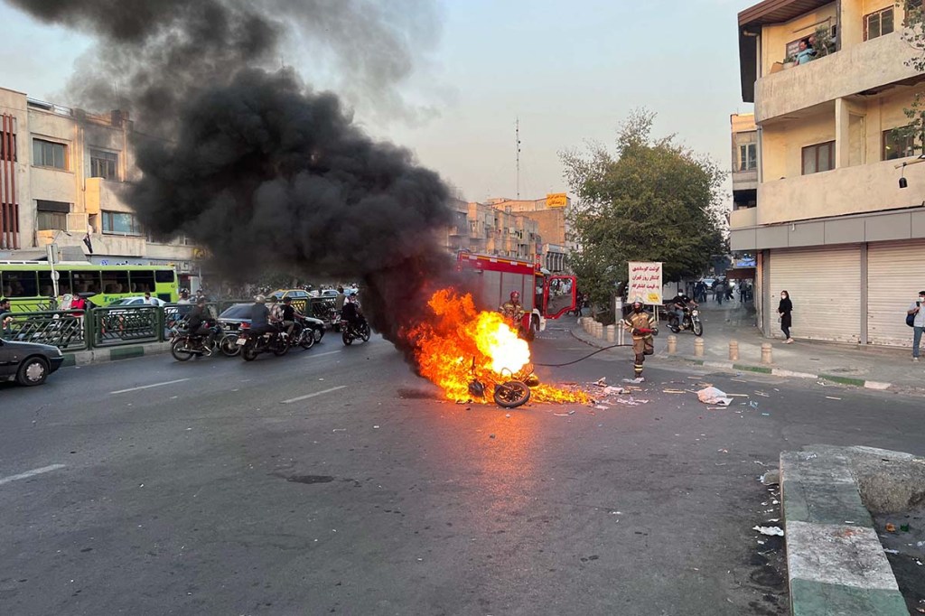 Ein Motorrad brennt mitten auf der Straße. Weitere Motorräder und Menschen sind um das aFeuer herum unterwegs.