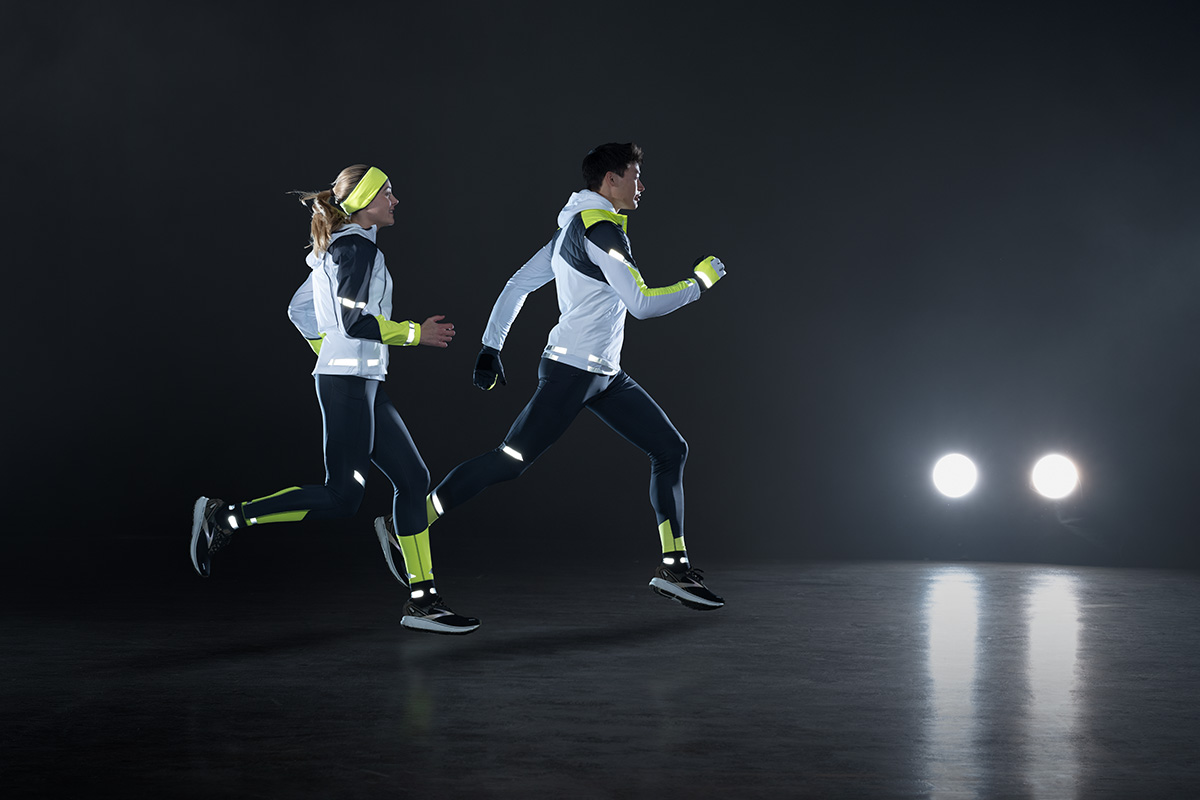Zwei Personen laufen im Dunkeln. Sie tragen die neue Lauf-Kollektion von Brooks. Im Hintergrund sind Autoscheinwerfer zu sehen.