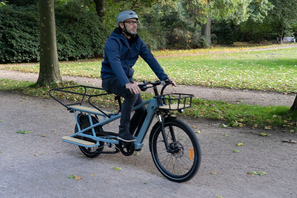 Mann fährt mit E-Cargo-Bike durch Parklandschaft
