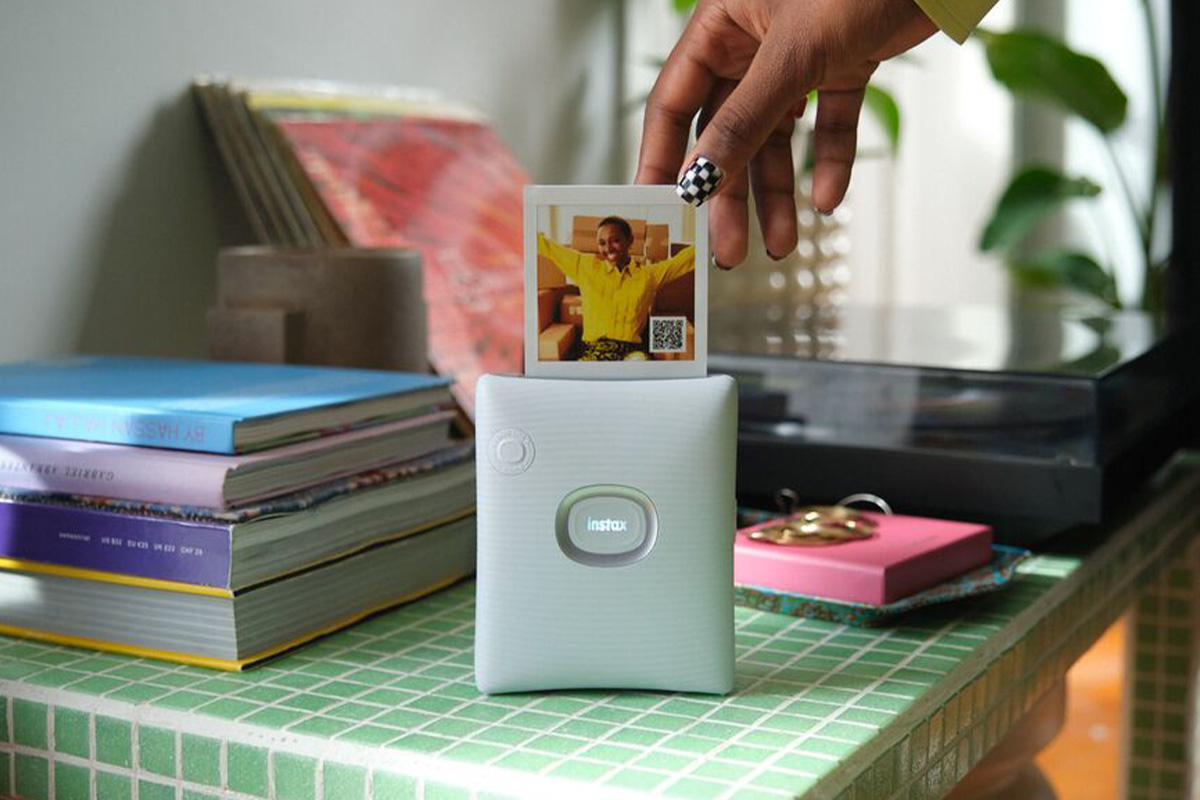 Der Fujifilm Instax Square Link druckt ein Fotos aus. Eine Hand nimmt es entgegen.