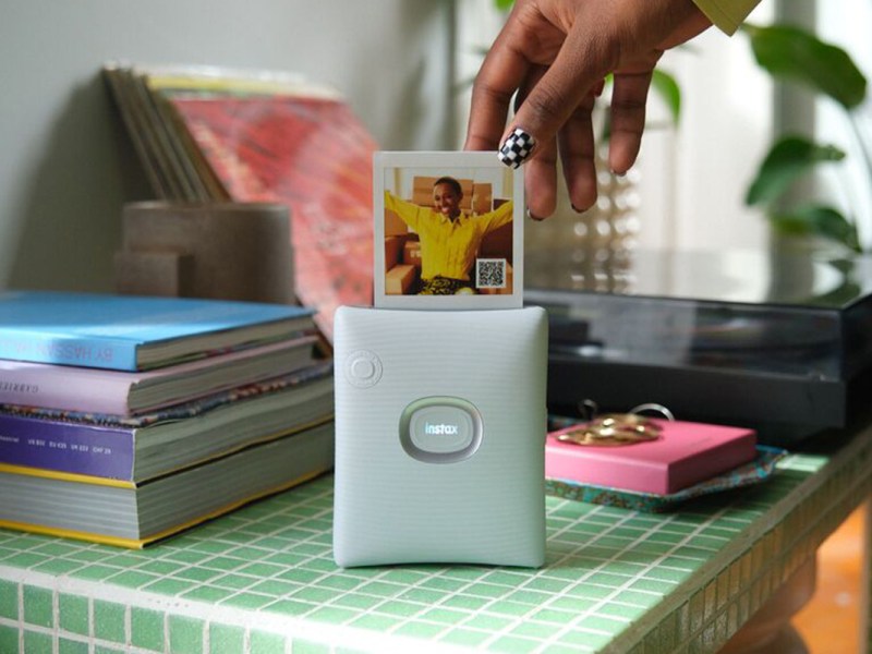 Der Fujifilm Instax Square Link druckt ein Fotos aus. Eine Hand nimmt es entgegen.