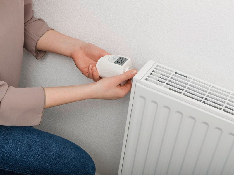 Eine Frau bedient ein smartes Heizkörperthermostat von Homematic IP.