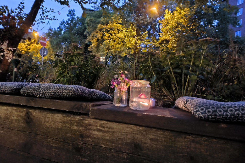 Aufnahme von Kerze im Glas auf Holzbank bei Nacht vor Gebüsch