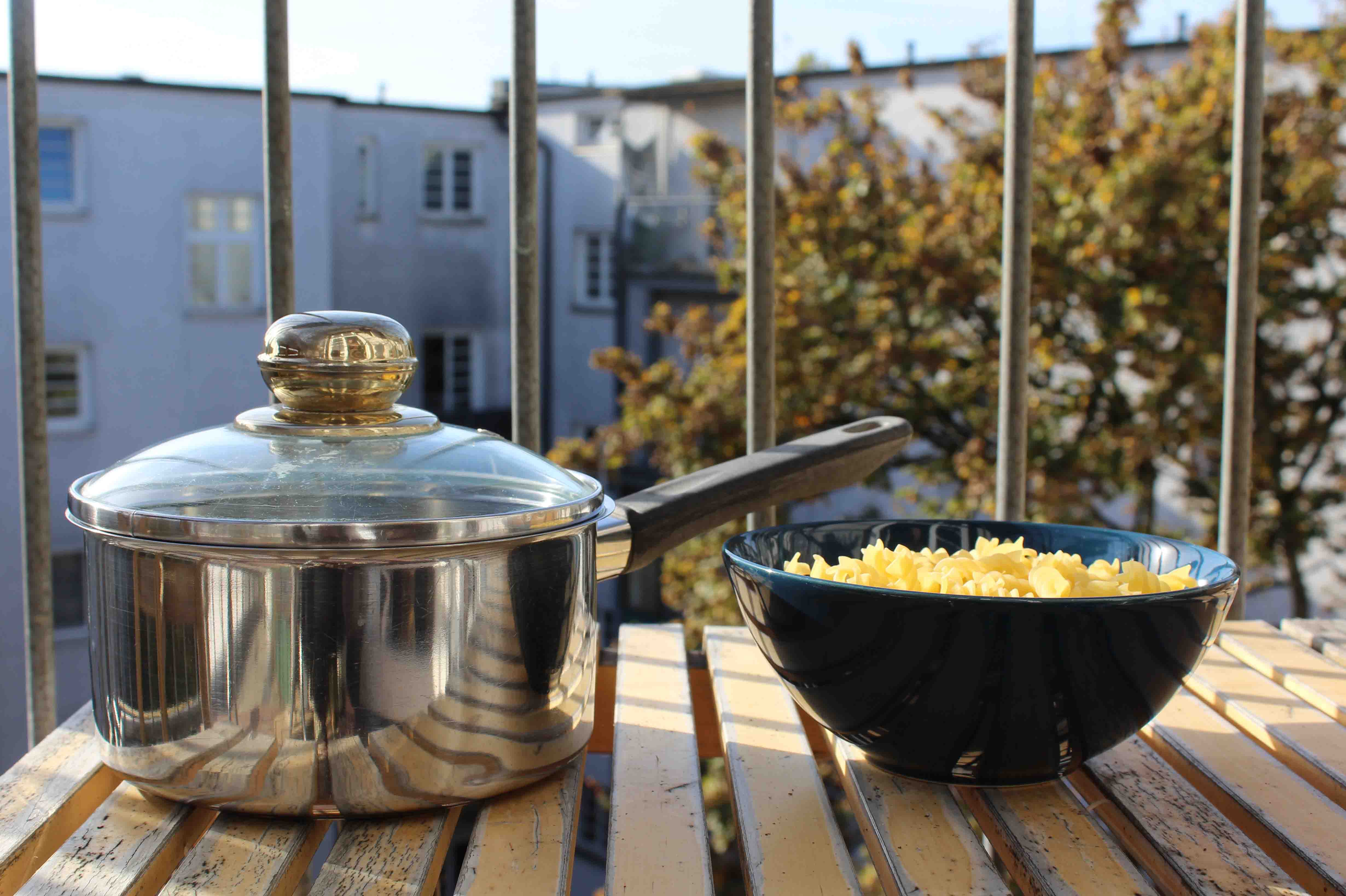 Ein Kochtopf mit Wasser und eine Schale mit Nudeln stehen auf einem Balkon.