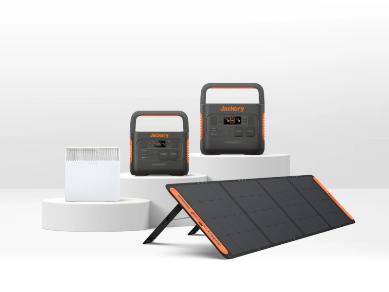 Schwarz orange Power Station von Jackery auf weißen Podesten mit weißer Elektroheizung davor und Solarpanel