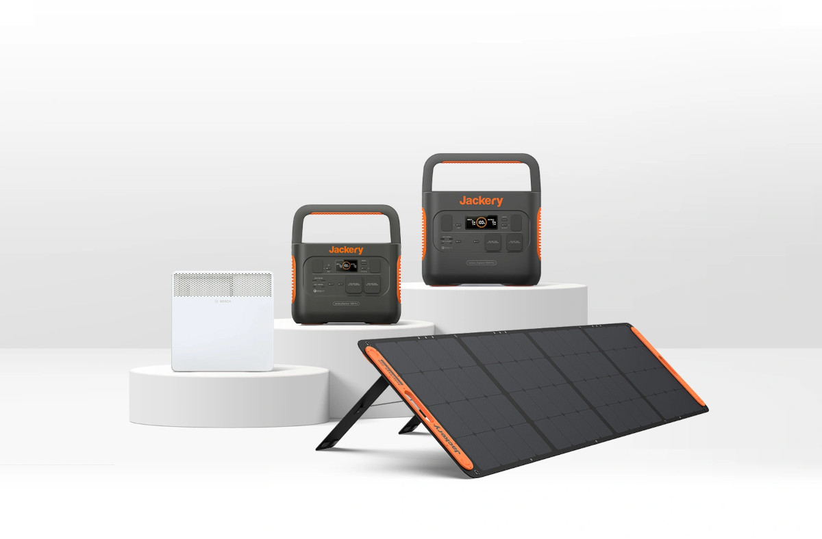 Schwarz orange Power Station von Jackery auf weißen Podesten mit weißer Elektroheizung davor und Solarpanel