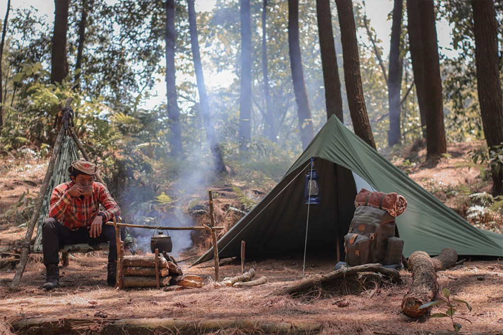 Mann im Wald mit Zelt und Kocher