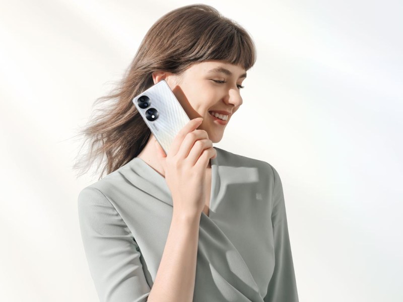 Eine brünette junge Frau vor einem hellen Hintergrund, die sich lächelnd das Honor 70 ans Ohr hält.