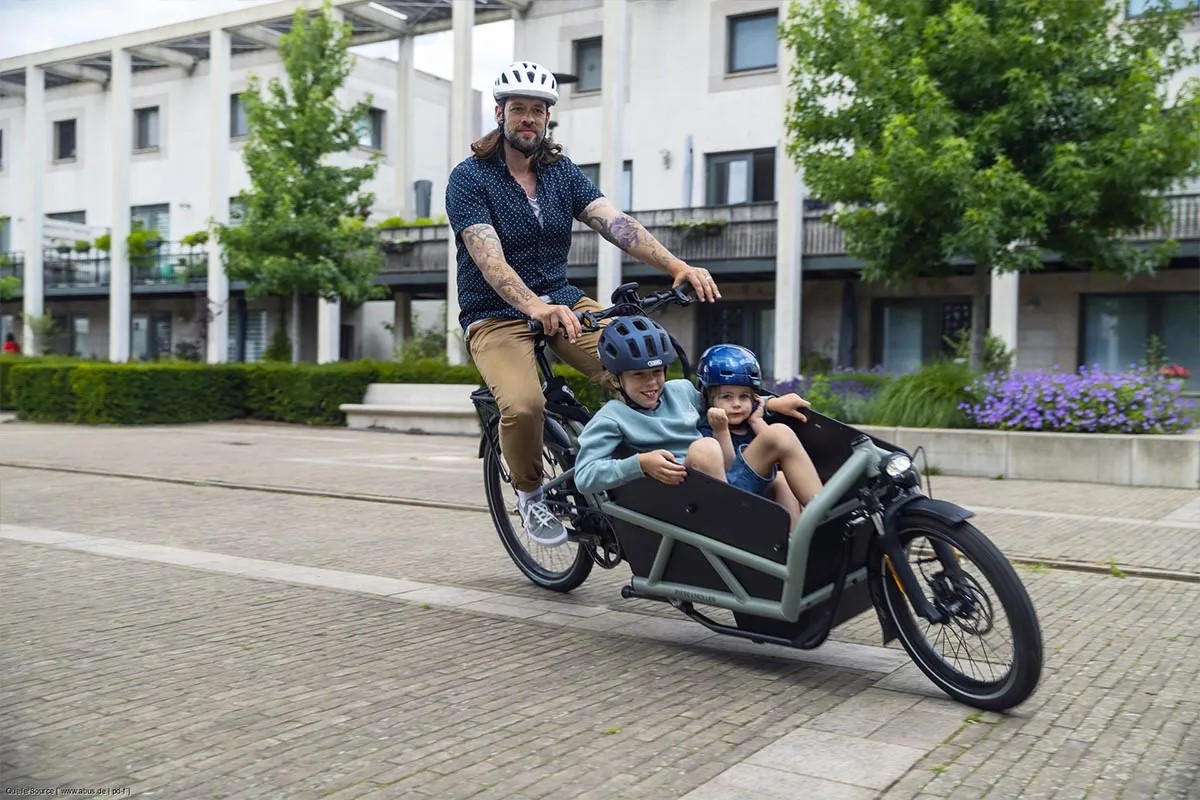 Mann fährt mit einem E-Cargo-Bike, im Lastenkorb sitzen zwei Kinder