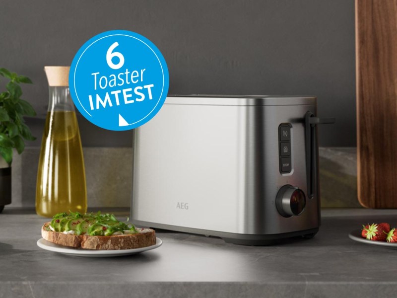 Silberner Toaster auf grauer Arbeitsplatte neben Flasche Öl und Teller mit blauem Button 6 Toaster IMTEST