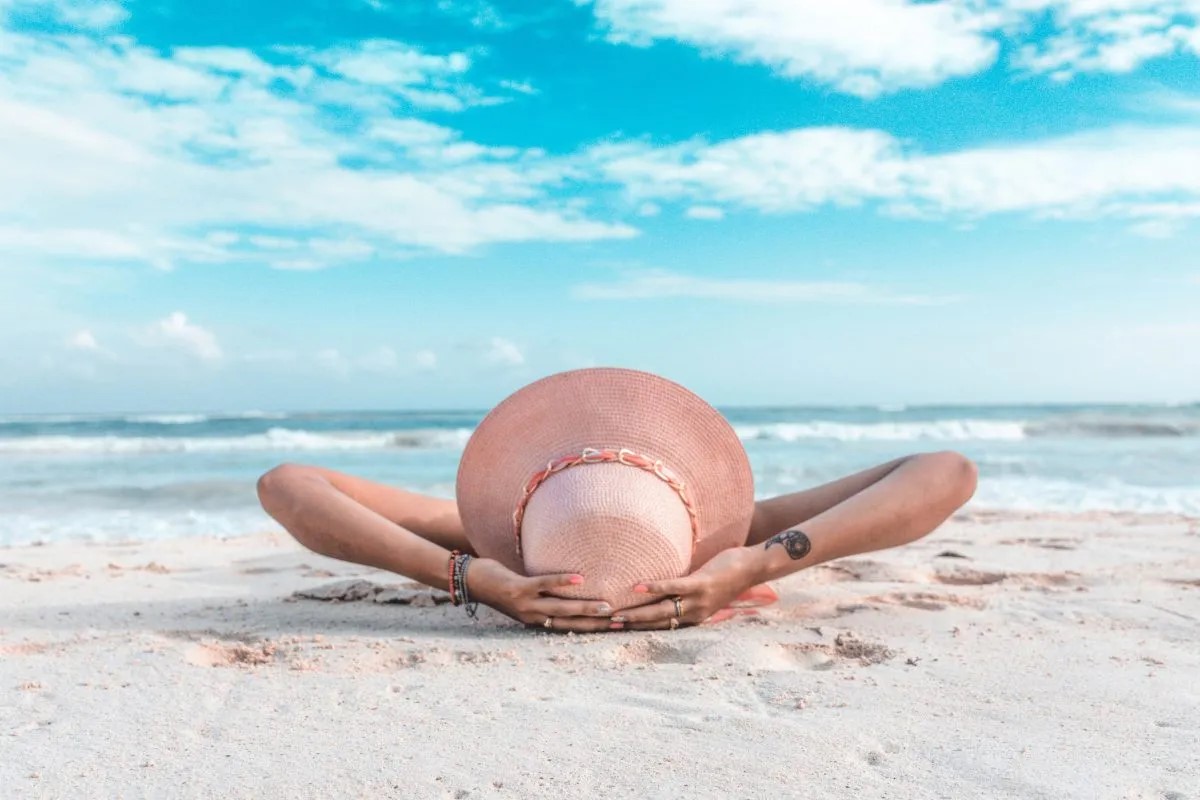 Eine Frau mit einem Sonnenhut liegt am Strand.