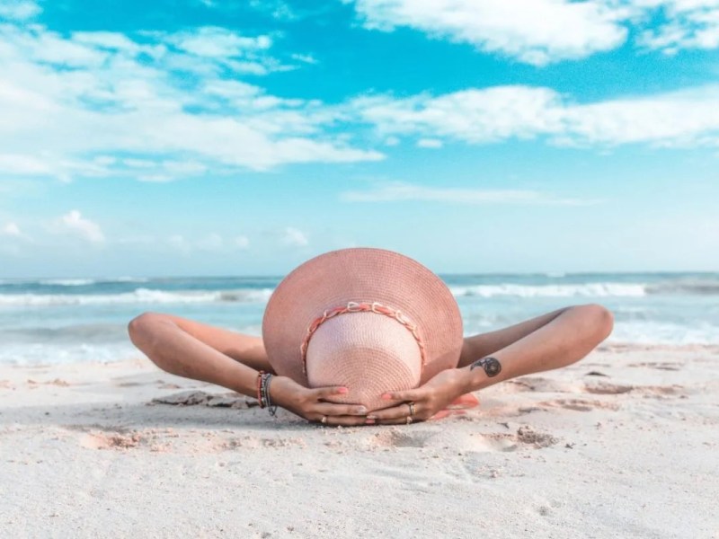 Eine Frau mit einem Sonnenhut liegt am Strand.
