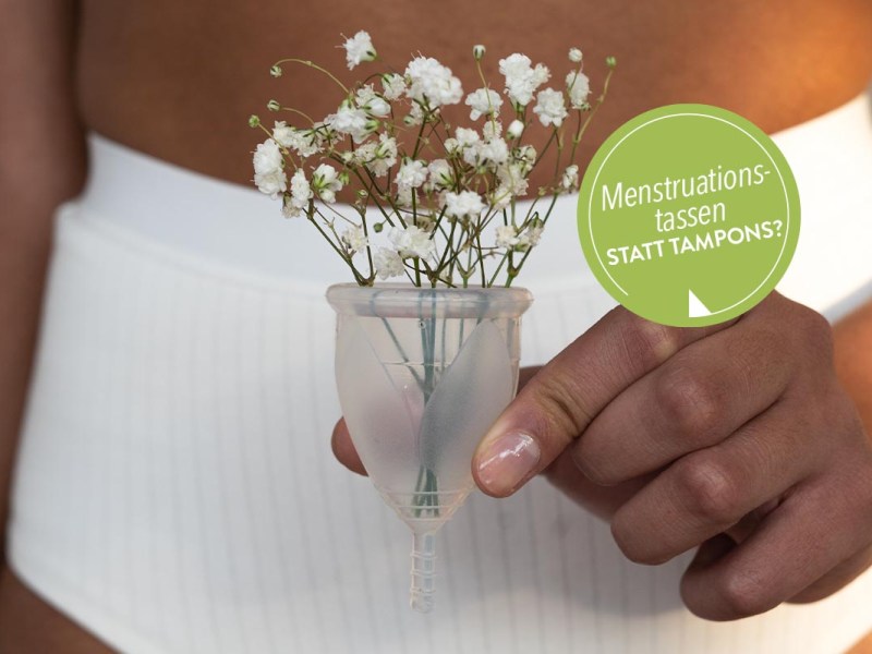 Frau hält Menstruationstasse in der Hand, in der sich Blumen befinden