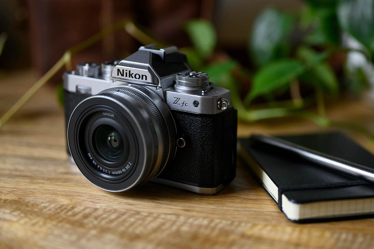 Die Nikon Z fc auf einem Hoilztisch neben einem Leder-Notizbuch