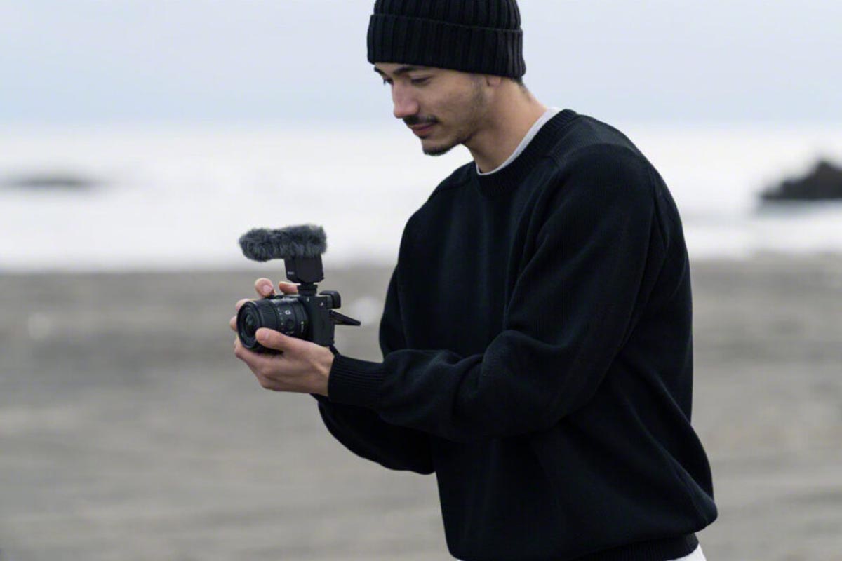 Ein Mann am Strand hält eine Sony-Kamera mit dem Weitwinkel-Objektiv