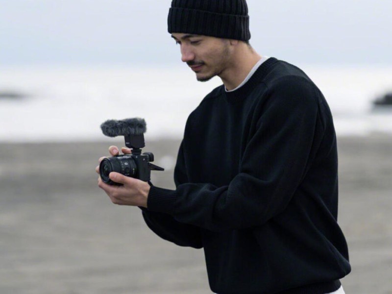 Ein Mann am Strand hält eine Sony-Kamera mit dem Weitwinkel-Objektiv