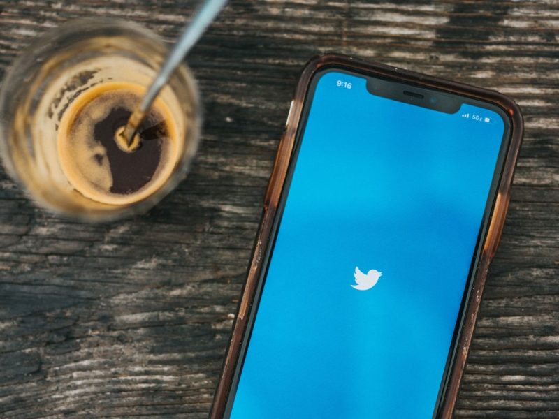 Ein Handy mit der Twitter-App liegt auf einem Holztisch neben einem Kaffee.