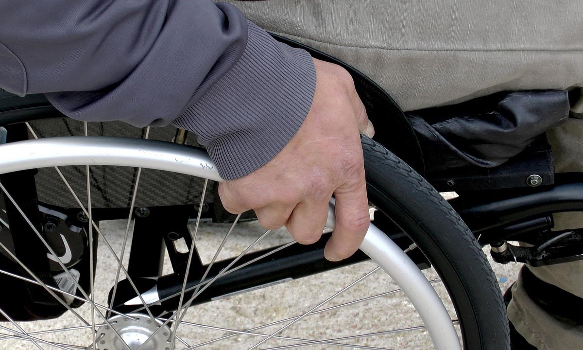 Detailaufnahme Hand am Rad eines Rollstuhls.