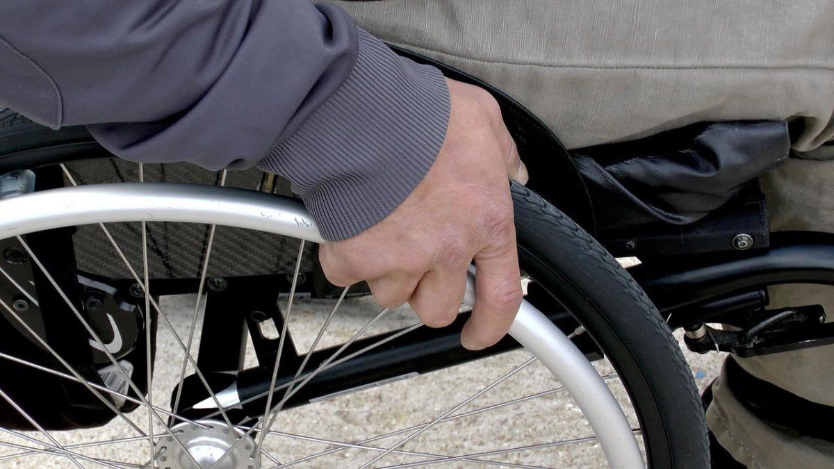 Detailaufnahme Hand am Rad eines Rollstuhls.