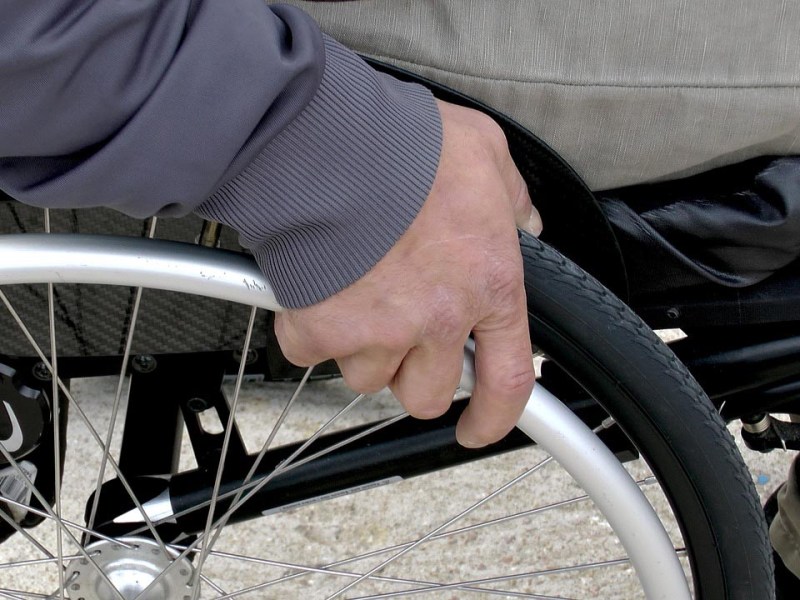 Detailaufnahme Hand am Rad eines Rollstuhls.