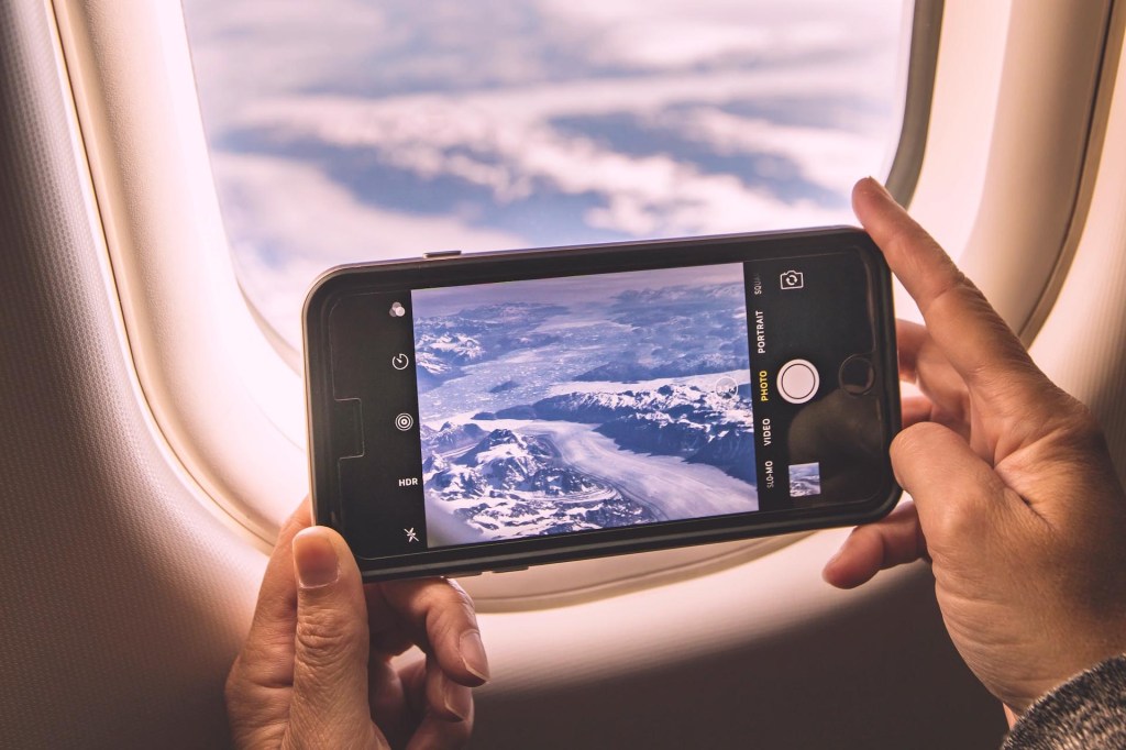 Person fotografiert aus Flugzeug heraus mit Smartphone (vermutlich im Flugmodus).