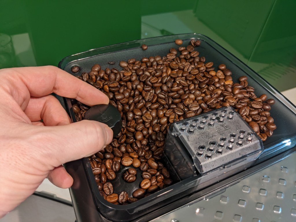 Hand an Behälter für Kaffeebohnen bei Kaffeevollautomat