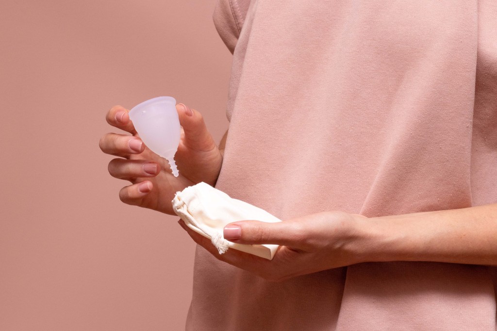 Eine Frau nimmt eine Menstruationstasse aus einer Hülle.
