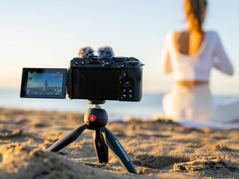 Die Z30 auf einem kleinen Stativ am Strand. Im unscharfen Hintergrund sitzt eine Frau in weißem Kleid
