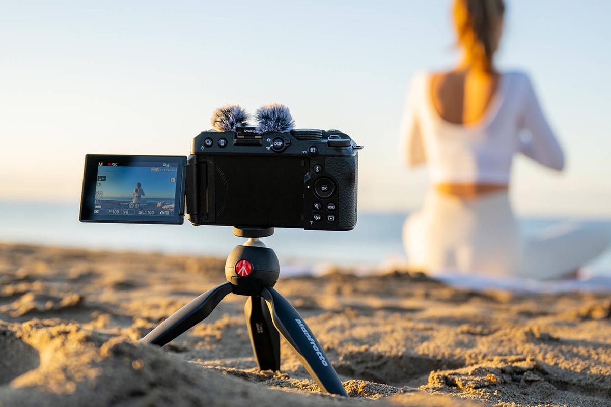 Die Z30 auf einem kleinen Stativ am Strand. Im unscharfen Hintergrund sitzt eine Frau in weißem Kleid