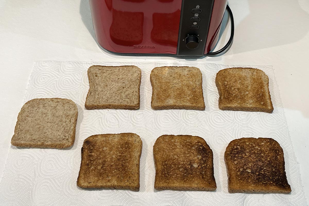 Sieben Toastscheiben unterschiedlich gebräunt, oben im Bild roter Toaster